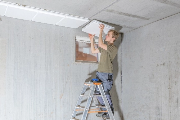 Person auf Leiter bringt Deckenplatten an